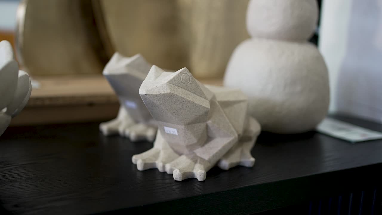 Two distinct geometric frog sculptures sit atop a dark surface in a modern decor shop. Their design brings a playful yet stylish touch to any space