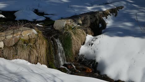 a shot of a tiny waterfall in the snow over a very low wall