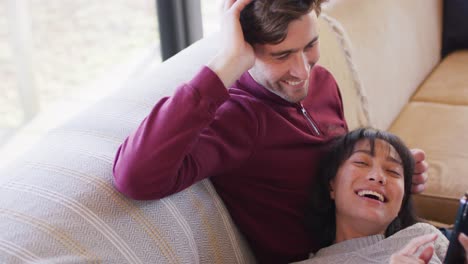 Video-of-back-view-of-happy-diverse-couple-sitting-on-sofa-and-talking