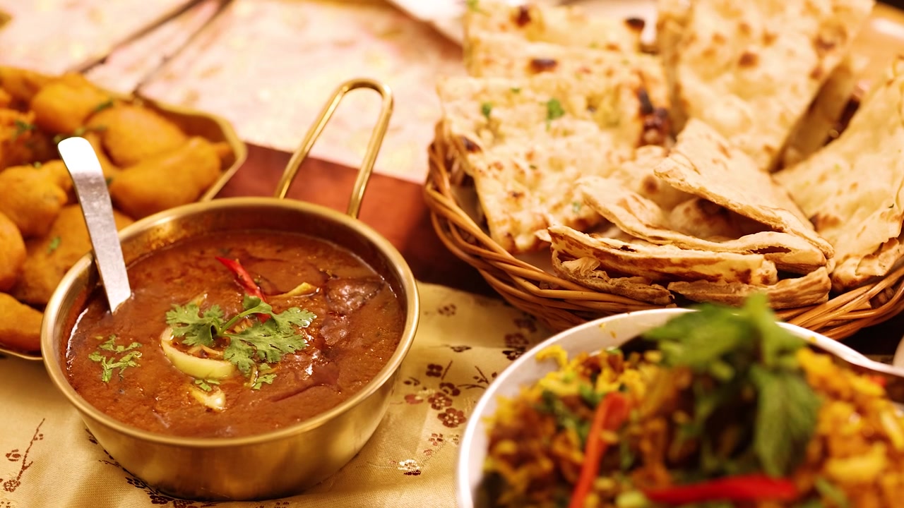 Langsom kamerapanorering hen over et bord fyldt med tandoori-kylling, naan og stærke saucer.