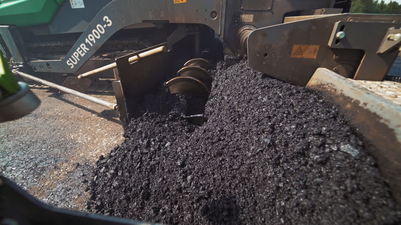 Metal construction of a heavy paver machine pouring out hot asphalt on the road. Asphalt spreader at work. Large truck laying black bitumen. Close-up.
