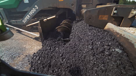 metal construction of a heavy paver machine pouring out hot asphalt on the road. asphalt spreader at work. large truck laying black bitumen. close-up.