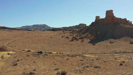 aerial follows car through rocky desert landscape on rugged dirt road