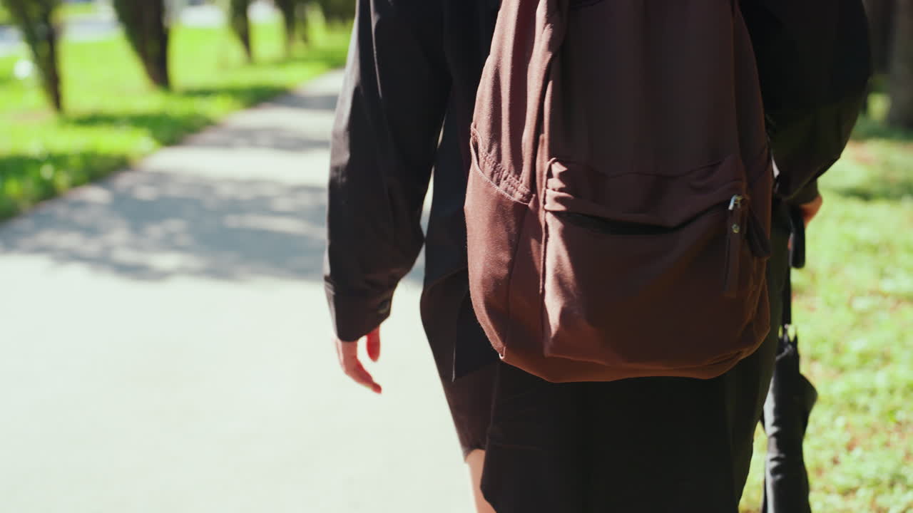 어떤 사람이 가방과 우산을 들고 푸른 숲 속을 떠납니다. 한 사람이 가방을 들고 그늘진 길을 따라 이동하며, 우산과 가방을 든 사람이 조용한 숲길을 따라 앞으로 나아갑니다.