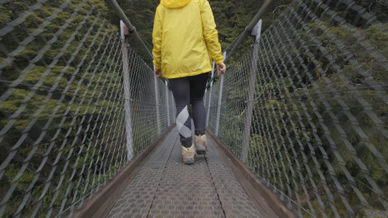 뉴질랜드의 다리를 건너는 노란색 재킷을 입은 소녀의 낮은 각도 샷