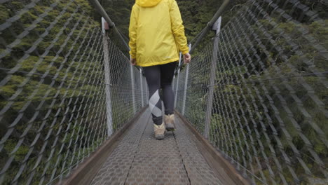 low angle shot of girl in yellow jacket walking across bridge in new zealand