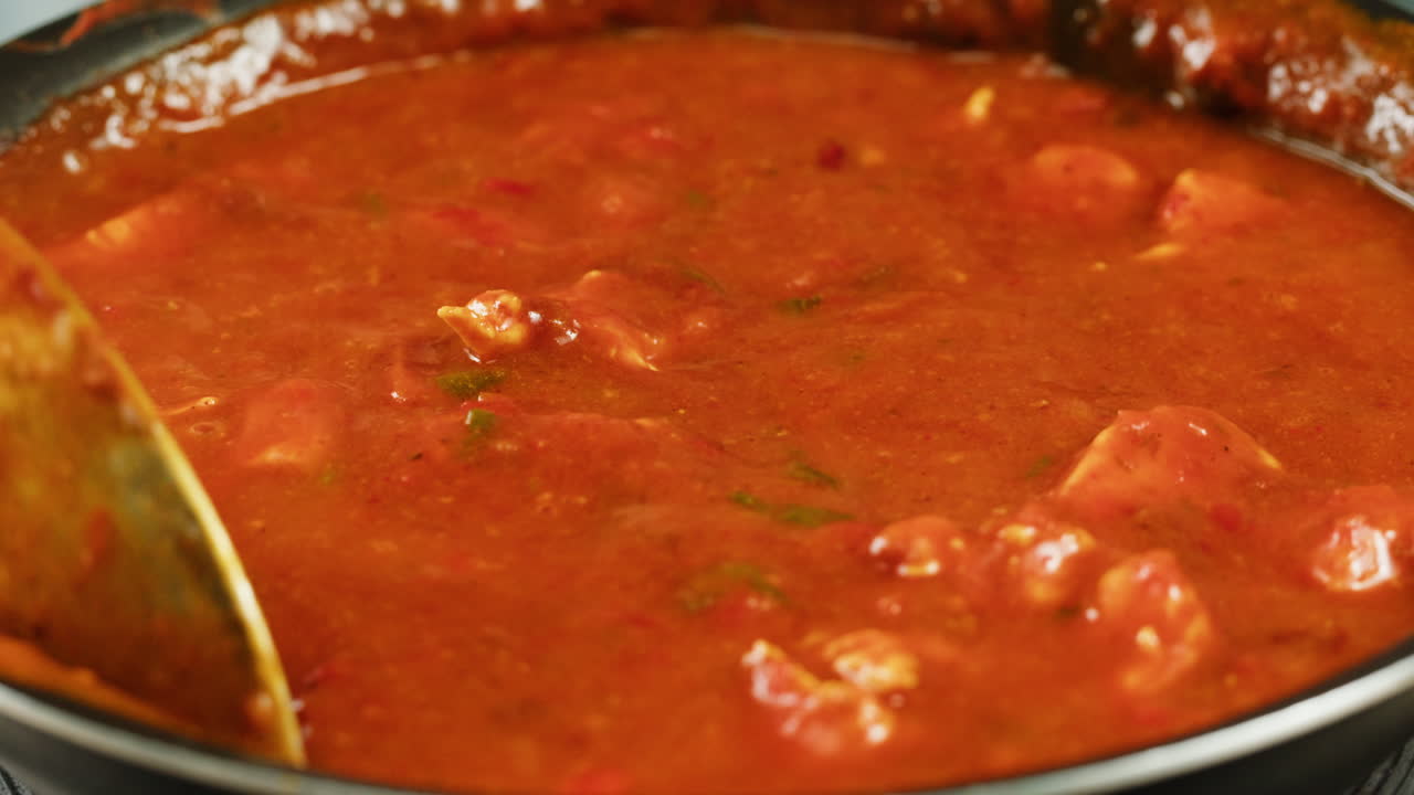 Chicken in tomato sauce is boiling on a frying pan with spices. Cooking tomato sauce curry with chicken fillet. Traditional Italian Mexican Asian dish. High quality studio shot for cafe, restaurant close up.