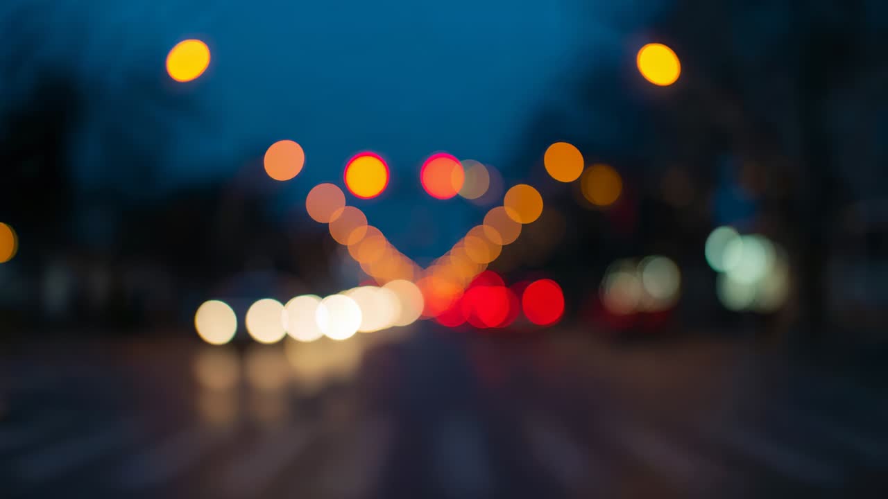Defocused suburban junction showing cars pausing at red signals departing with shifting light bokeh