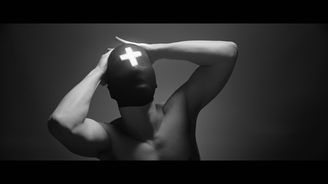 Masked man with cross of light glowing on his face moves slowly