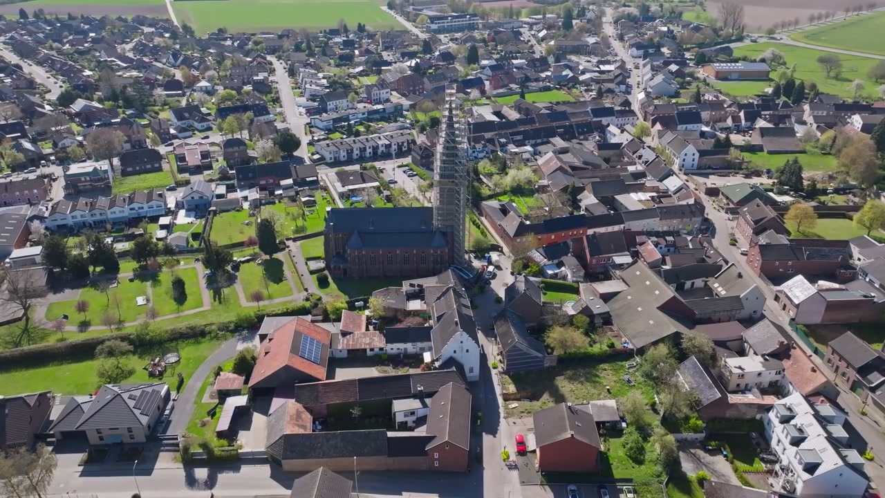 Luftdrone som sirkler rundt historisk kirke under oppussing med stillaser som viser restaureringsarbeid på eksteriøret av en gammel religiøs bygning i en europeisk by på dagtid.