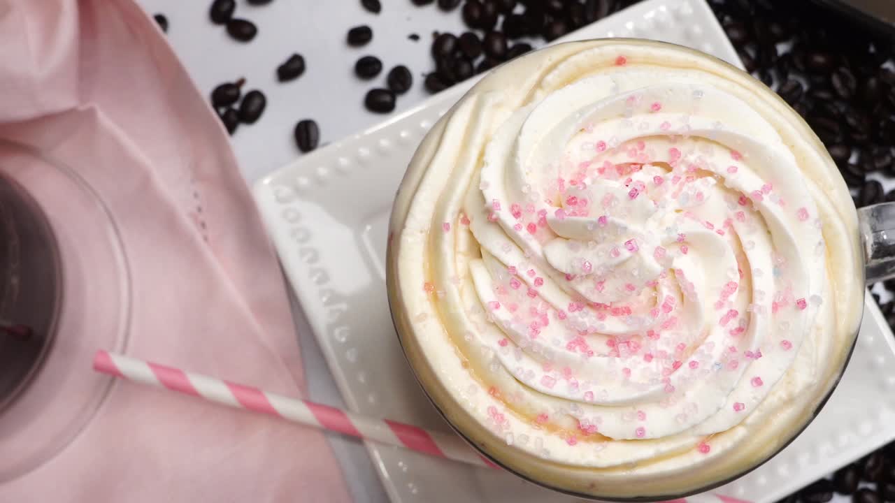 Dessert pink coffee in a mug topped with whipped cream and sugar sprinkles. Delicious and sweet dessert hot coffee in a coffee mug and surrounded by coffee beans.