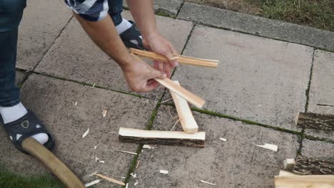 Young man is chopping wood in smaller pieces and putting it aside