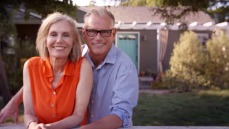 Portrait-Of-Mature-Couple-Looking-Over-Back-Yard-Fence