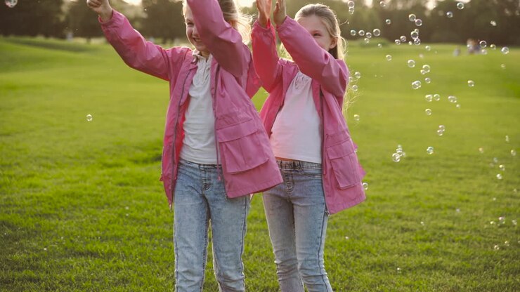 Sorelline felici con vestiti identici che acchiappano bolle di sapone nel parco 3