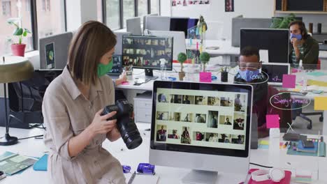 mujer de negocios caucásica con máscara facial usando una cámara en una oficina moderna
