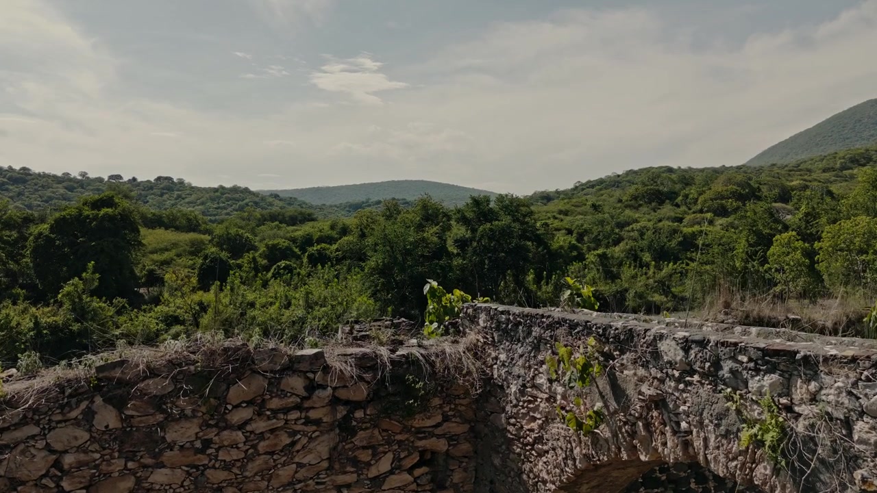 Rovine di acquedotto in pietra con muri in muratura ad arco, terreno asciutto, albero e colline boscose, seguite da vegetazione verde e canale d'acqua in cemento a Ixtoluca, Morelos, Messico