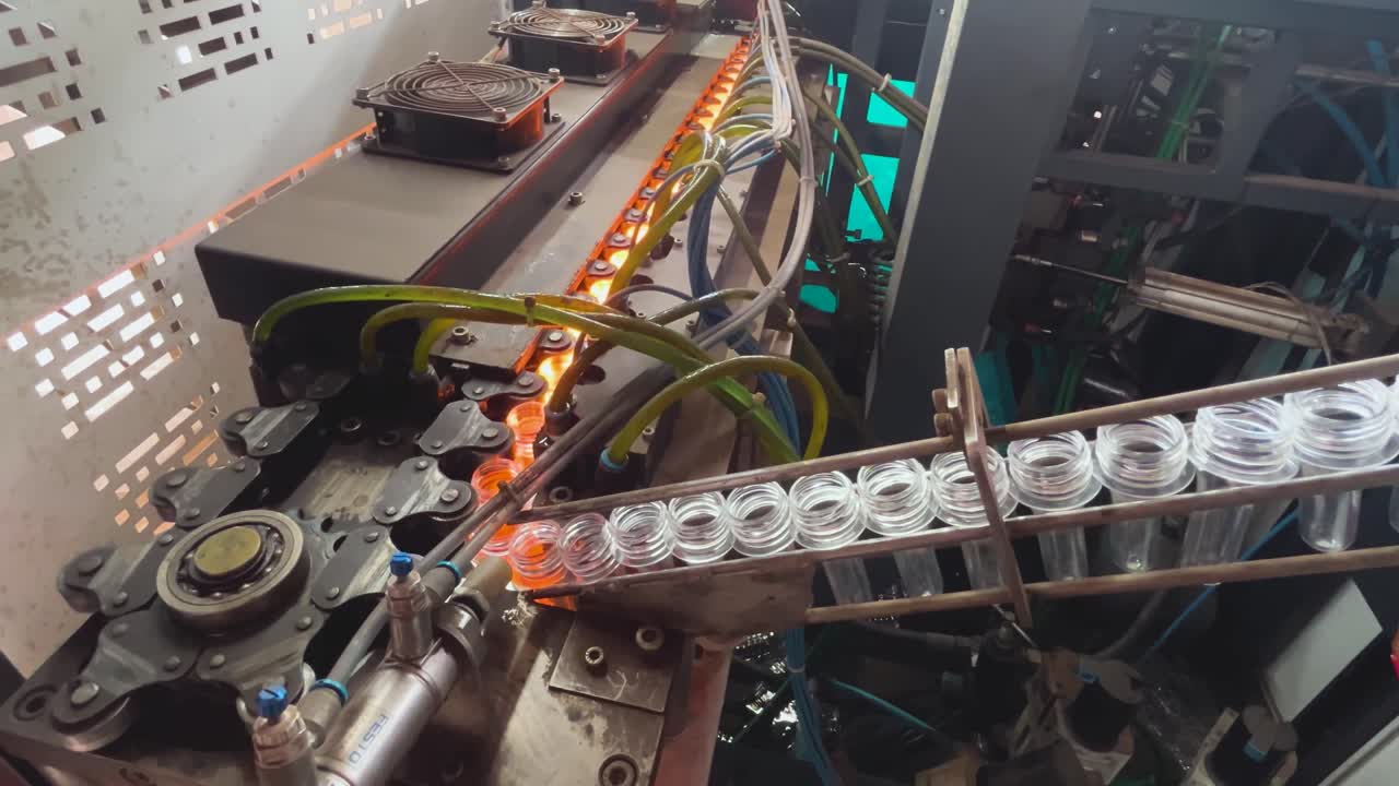 Working of a PET bottle blowing machine in which mechanised chain carrying preforms