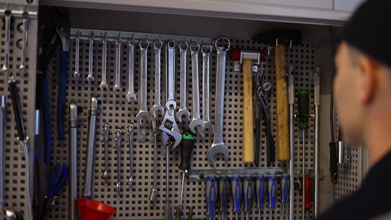 A car mechanic stands near the stand with wrenches, take the required size