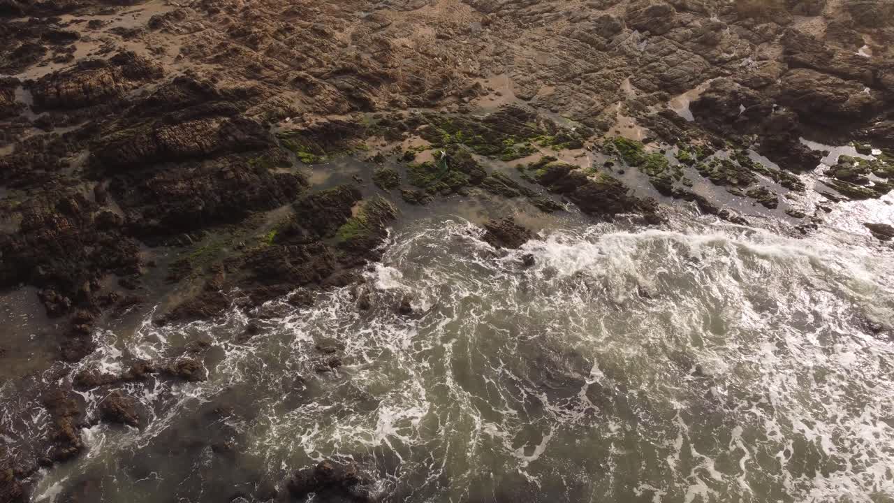 surfista caminando sobre rocas entrando al mar en el océano atlántico en la playa de punta del este