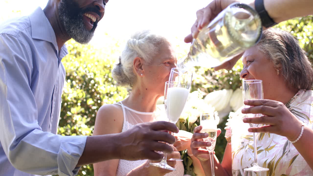 Amici anziani versano champagne e festeggiano a un matrimonio all'aperto, godendosi la compagnia reciproca.