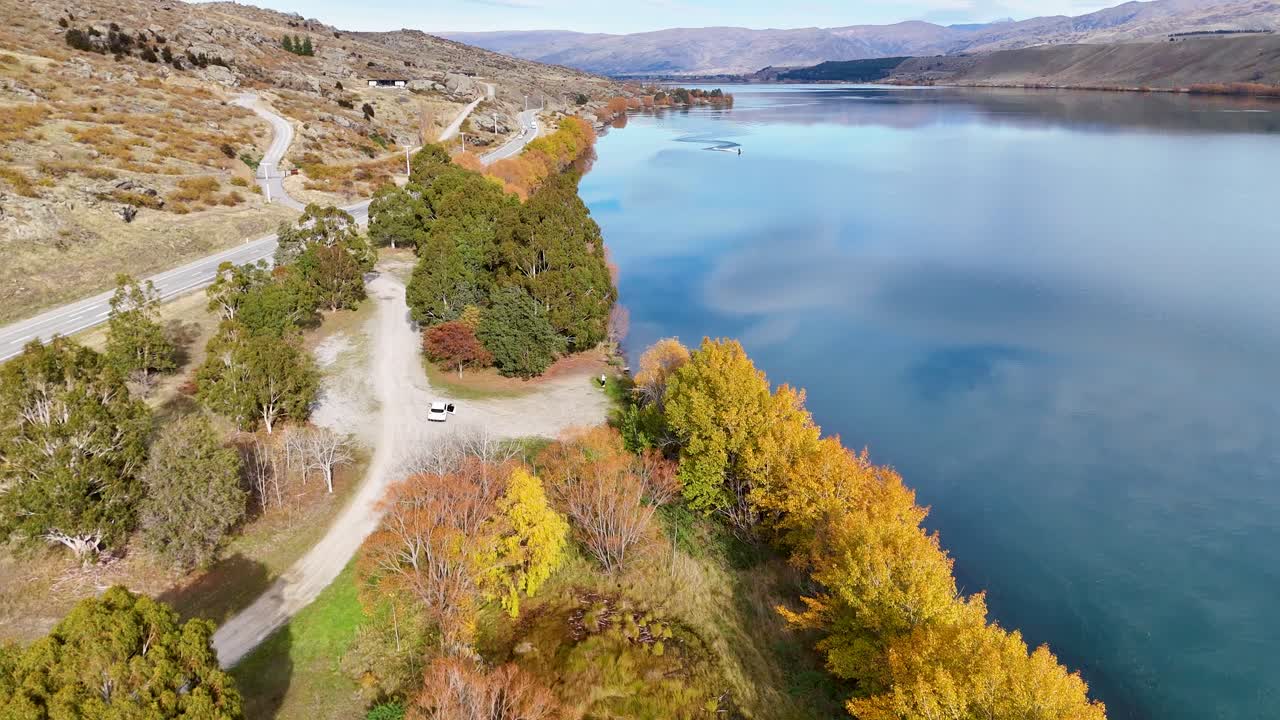Drone footage captures Lake Dunstan's vibrant autumn colors and serene waters in Cromwell, New Zealand, highlighting the natural beauty and tranquility