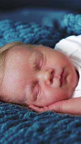 adorable caucasian newborn peacefully sleeping. cute baby put a hand under his cheek sleeps on his side covered in blue woven blanket. close up. vertical video