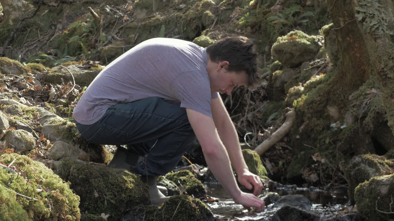 Young man washes face in woodland brook, stream, creek