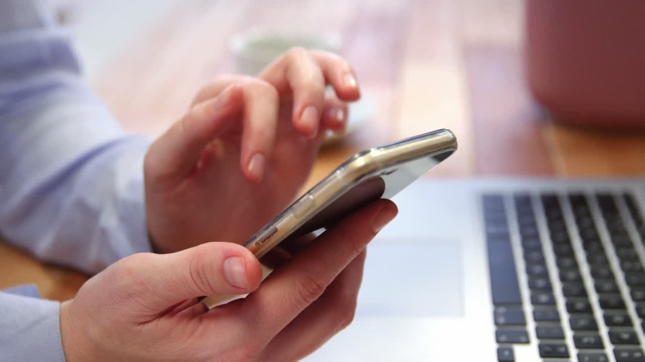 mujer usando un teléfono móvil mientras trabaja en una computadora portátil en el escritorio