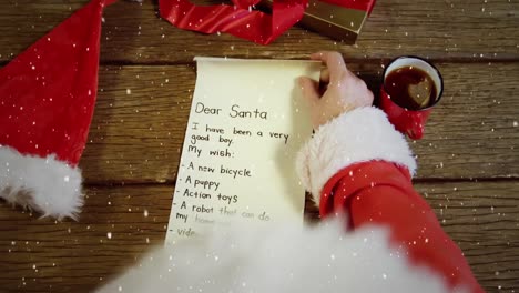 Video-composition-with-falling-snow-over-santa--looking-at-wish-list-top-view