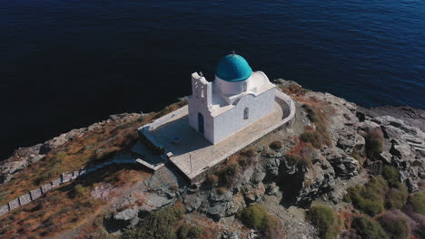 aerial shot of a greek orthodox blue dome chapel built on a cliff overlooking the aegean sea