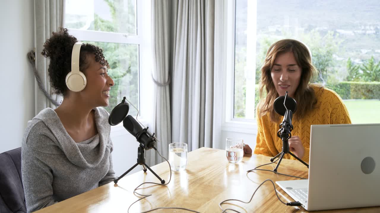 Copresentadoras diversas ajustándose los auriculares e introduciendo un tema en el micrófono mientras asienten en casa.
