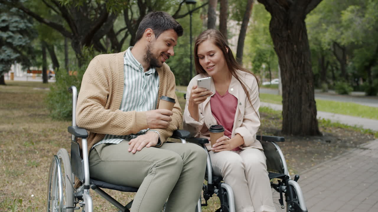 Couple in Wheelchairs Enjoying Coffee and a Phone Conversation in a Park