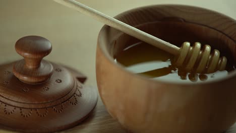 miel en un cuenco de madera profundo, plato de madera rústico. la cuchara de madera gotea lentamente.