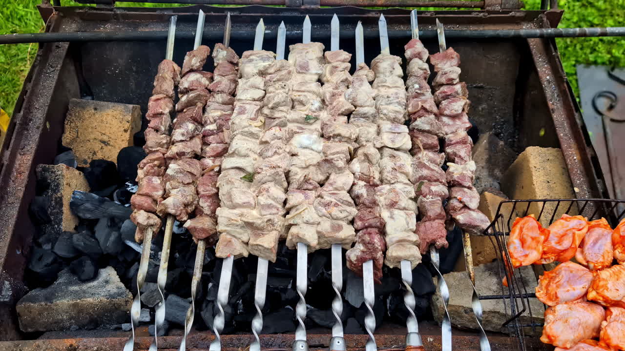 Griglia con file di spiedini di carne che cuociono all'aperto di giorno durante un barbecue estivo.