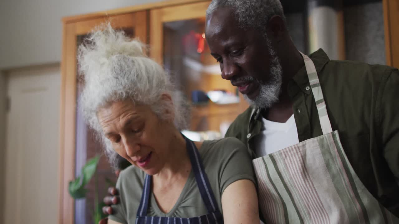 Mixed race couple wearing aprons talking to each other in the kitchen at home