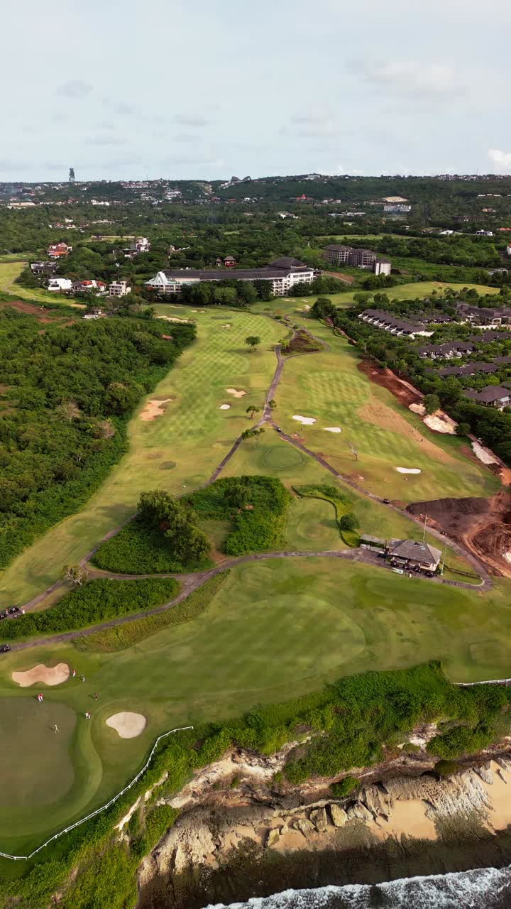 Vertical drone video capturing a cliffside golf course above crashing ocean waves with tropical coastal vegetation and limestone cliffs creating a striking sports and nature landscape scene