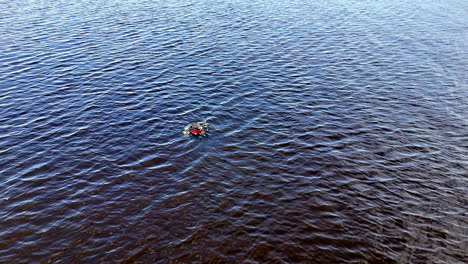 A lone diver drifts in the middle of a large, dark waterbody. Surrounded by rippling waves and empty space, the moment captures solitude, immersion, and human vulnerability in nature