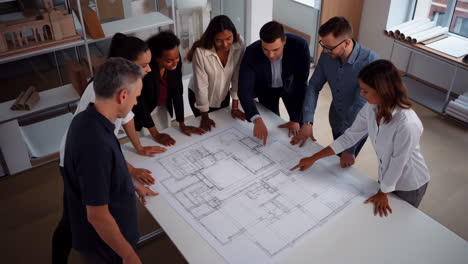 diverse team of architects and engineers discussing blueprints in an office meeting