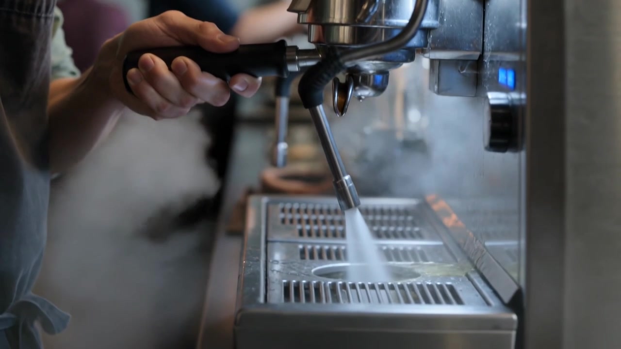 Leaning barista in dark apron green top at espresso machine, aligning portafilter, opening steam