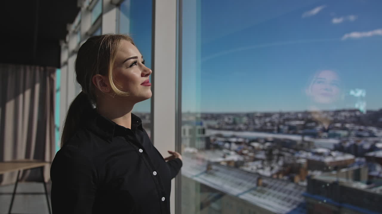 Attractive female enjoying the sunrays coming through the big panoramic window. Great look at the city from the office center. Close up with gradual distancing.