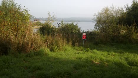 Grass-waters-edge-of-Carsington-Water-with-the-Water-Valve-Tower,-Draw-Off-Tower-in-the-Background