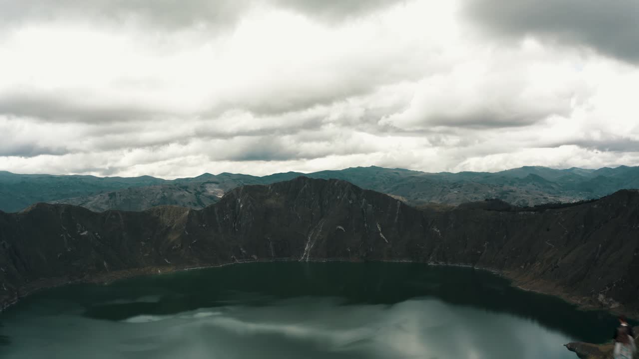 drone vuela sobre el lago quilotoa con gente en la cima de una colina en ecuador