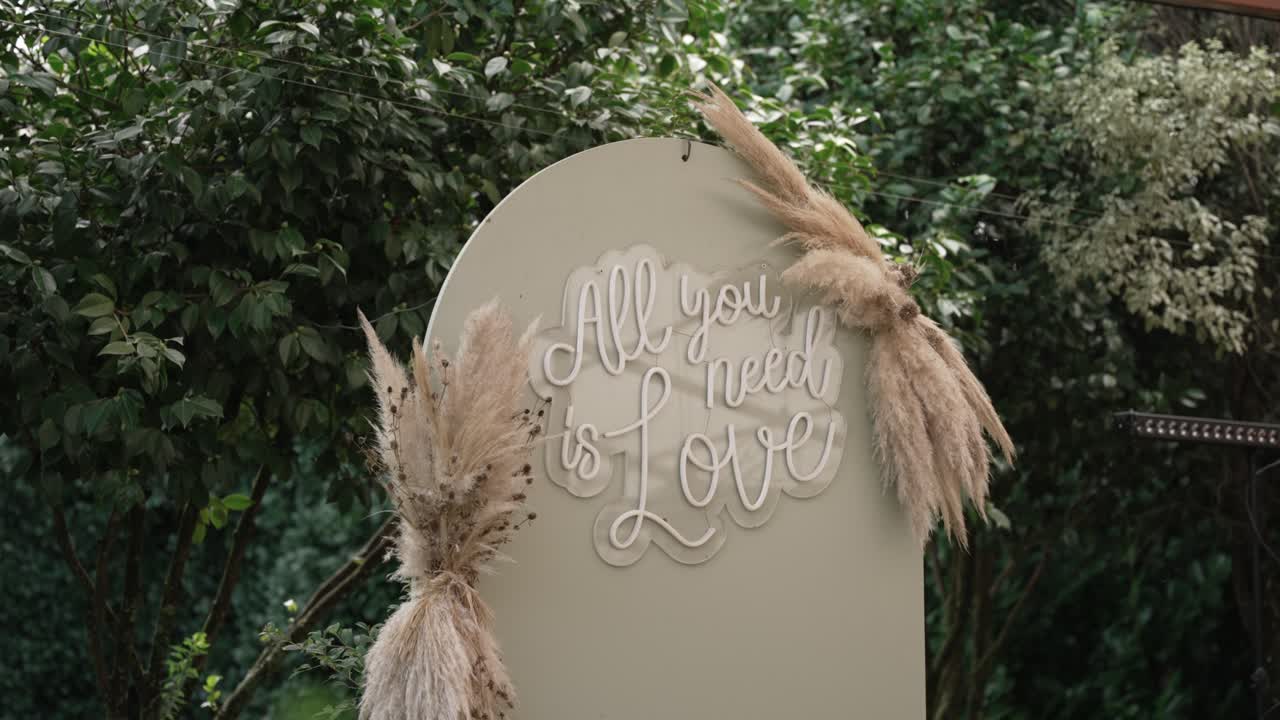 Decorative wedding sign with pampas grass and quote "All you need is love" outdoors