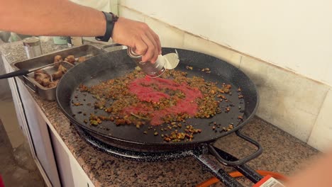 persona está agregando aditivo culinario a una gran sartén de metal, preparando y cocinando concepto de alimentos