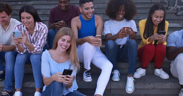 Diverse Group of Young Friends Using Smartphones and Laughing Outdoors