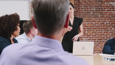 young businesswoman standing and leading office meeting around table