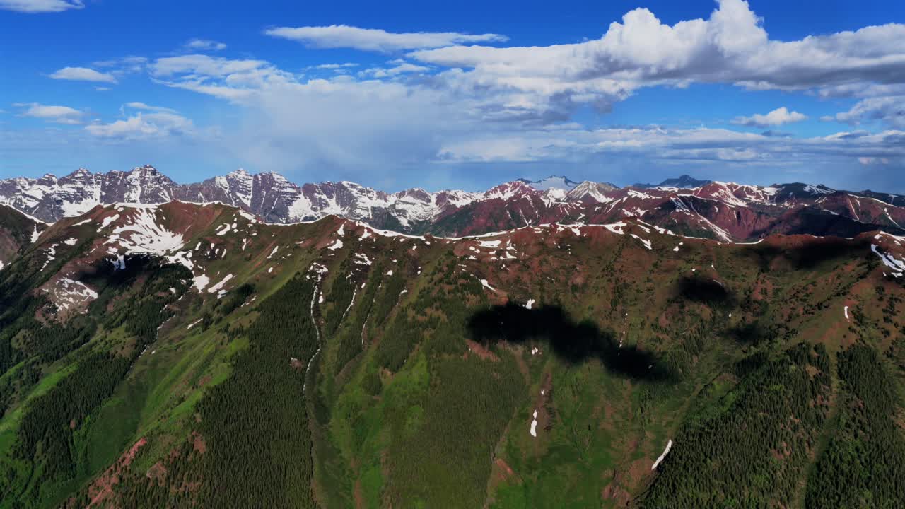 Summit Aspen Highlands bowl spring summer Maroon Bells Wilderness Pyramid Peak Elk Mountain Range aerial drone Colorado Snowmass Mountain Capitol Peak 14er sunny morning blue sky clouds backwards
