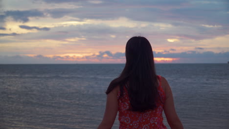 Rückansicht-Einer-Frau,-Die-Einen-Spektakulären-Sonnenuntergang-Mit-Bewölktem,-Dramatischem-Himmel-Und-Farbenfrohen-Reflexionen-Auf-Dem-Meer-Bewundert