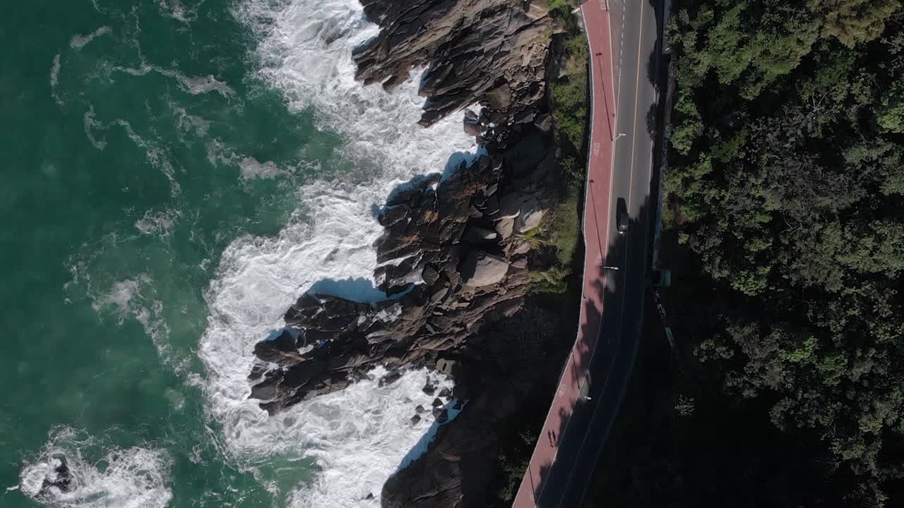 antena de arriba hacia abajo siguiendo la avenida niemeyer de la costa con un amplio carril bici a un lado de las olas rompiendo en la playa de rocas