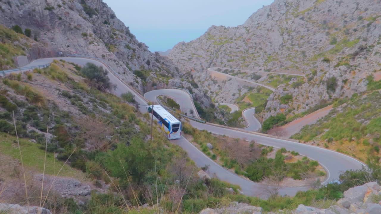 un autobús y un coche se mueven por una estrecha carretera en zigzag en las montañas con bosques frondosos en los inviernos en mallorca, españa